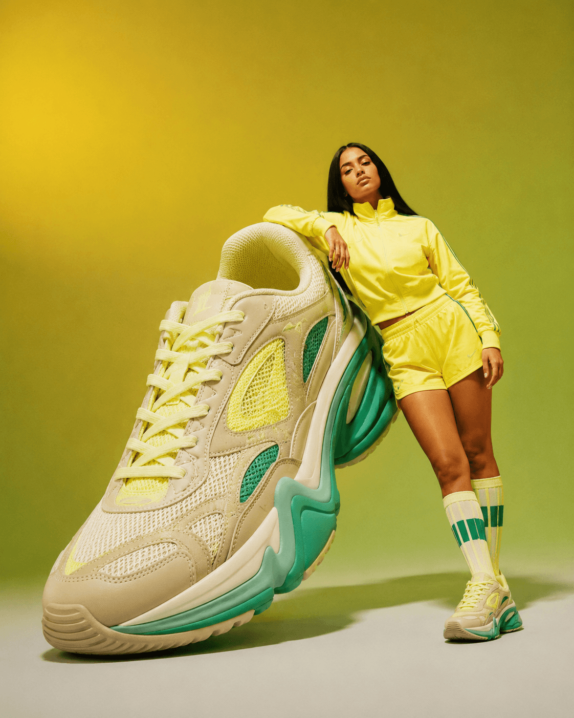 Model leaning against an oversized sneaker on a yellow and green studio backdrop